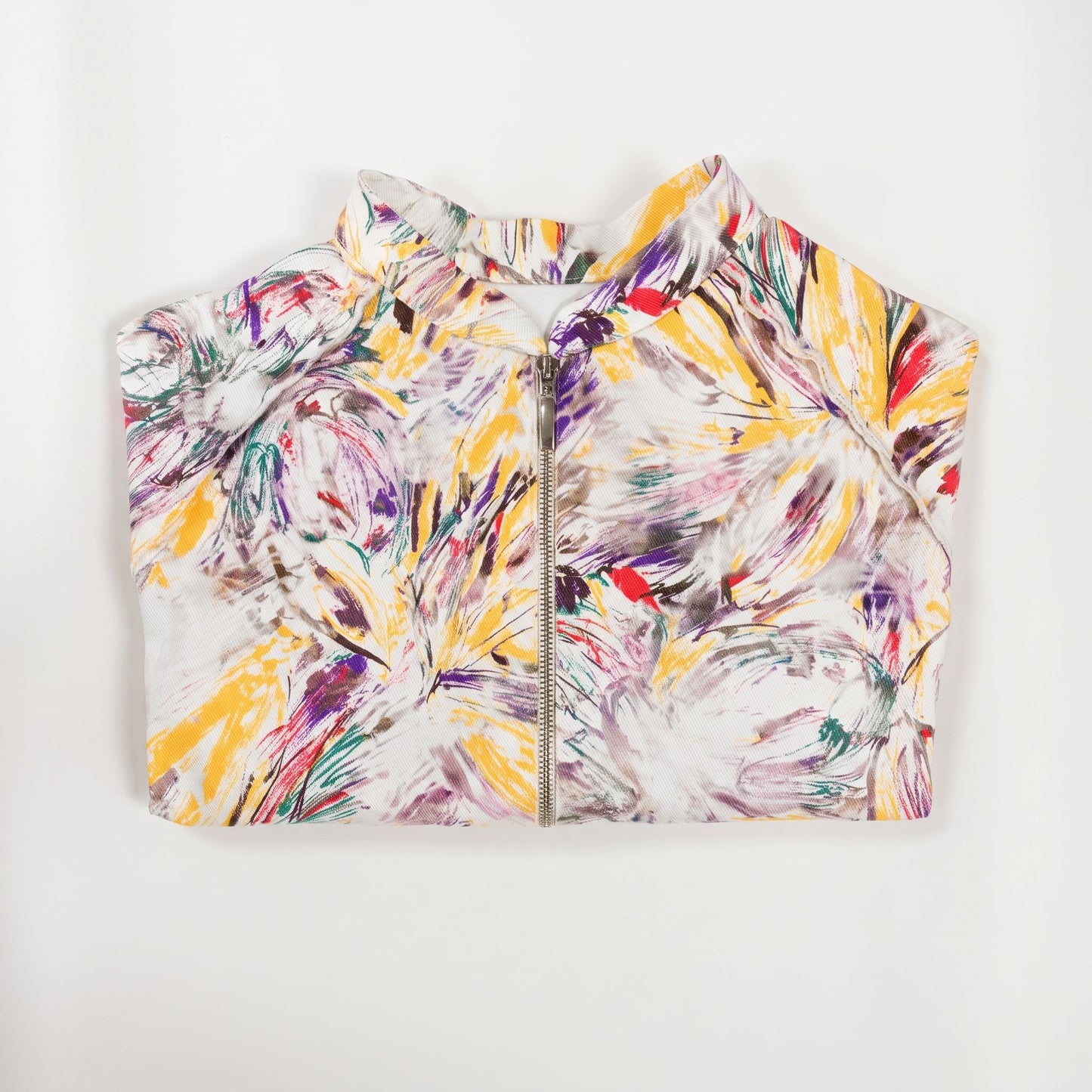 Giacca corta artigianale da donna con stampa artistica multicolore su fondo bianco, collo alto, maniche raglan e chiusura frontale con zip, vista piegata.
