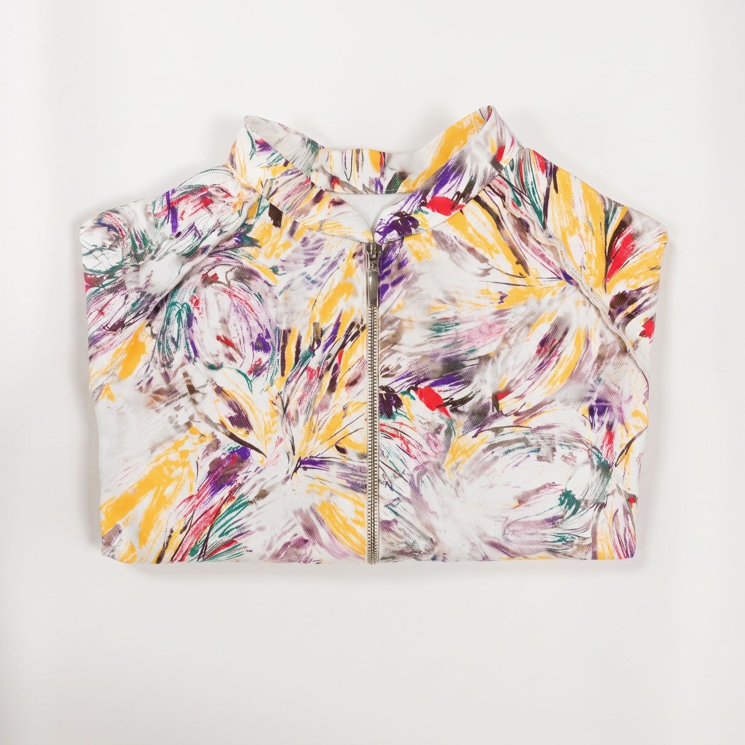 Giacca corta artigianale da donna con stampa artistica multicolore su fondo bianco, collo alto, maniche raglan e chiusura frontale con zip, vista piegata.