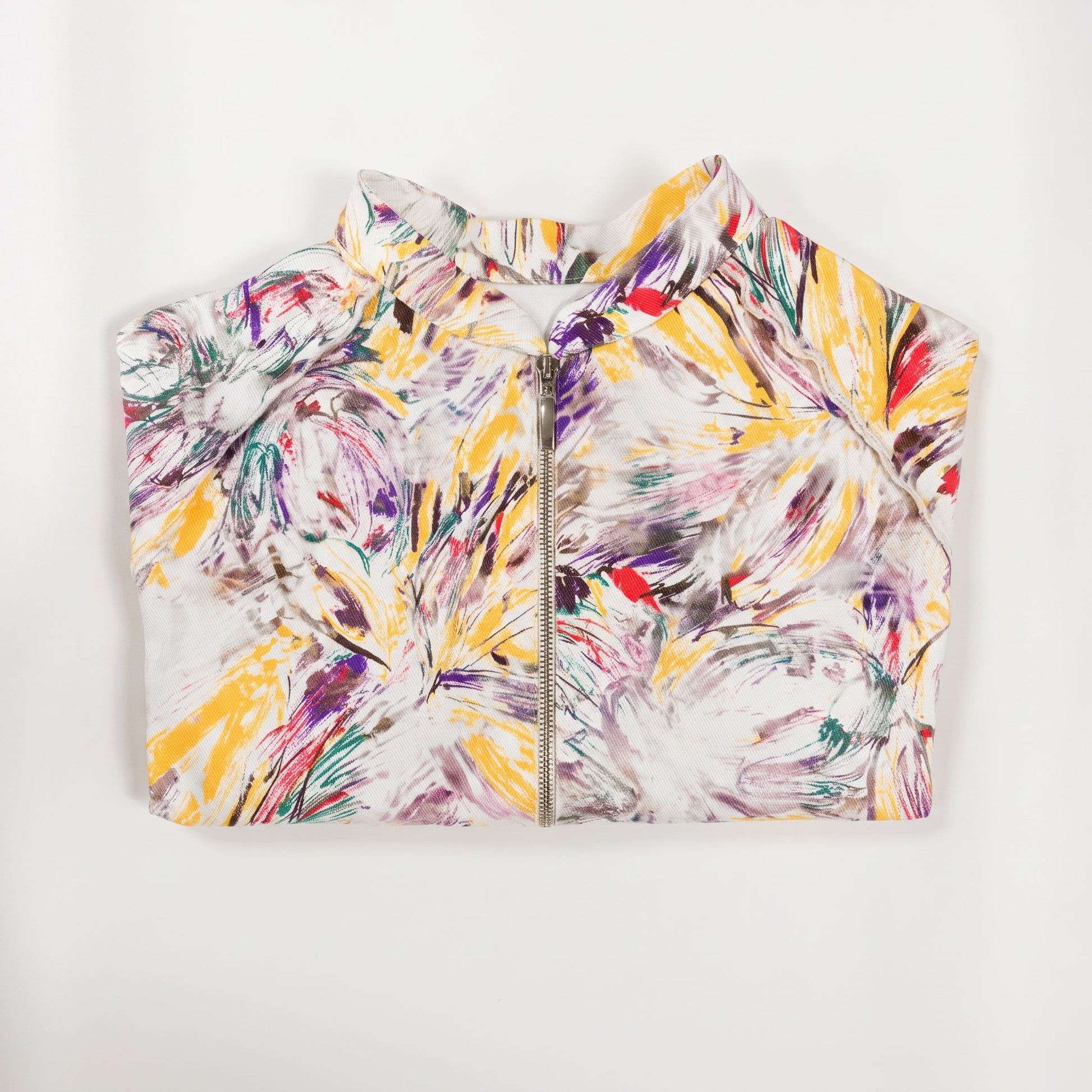 Giacca corta artigianale da donna con stampa artistica multicolore su fondo bianco, collo alto, maniche raglan e chiusura frontale con zip, vista piegata.